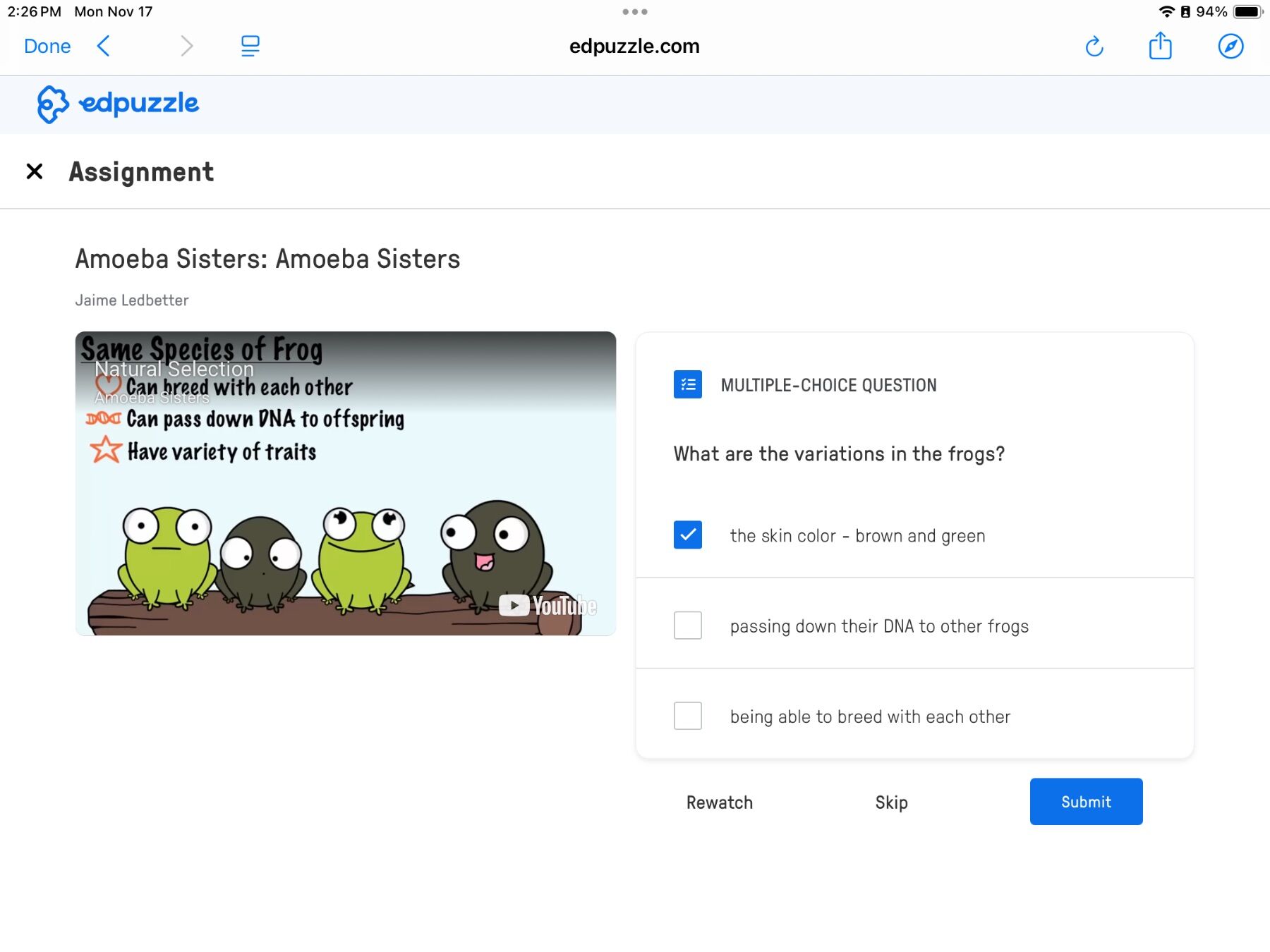 Screenshot of an Edpuzzle assignment featuring "Amoeba Sisters: Amoeba Sisters" with a video thumbnail of cartoon frogs in brown and green. Text highlights traits like DNA passing and variety. A multiple-choice question asks about variations in the frogs, with "the skin color - brown and green" checked.